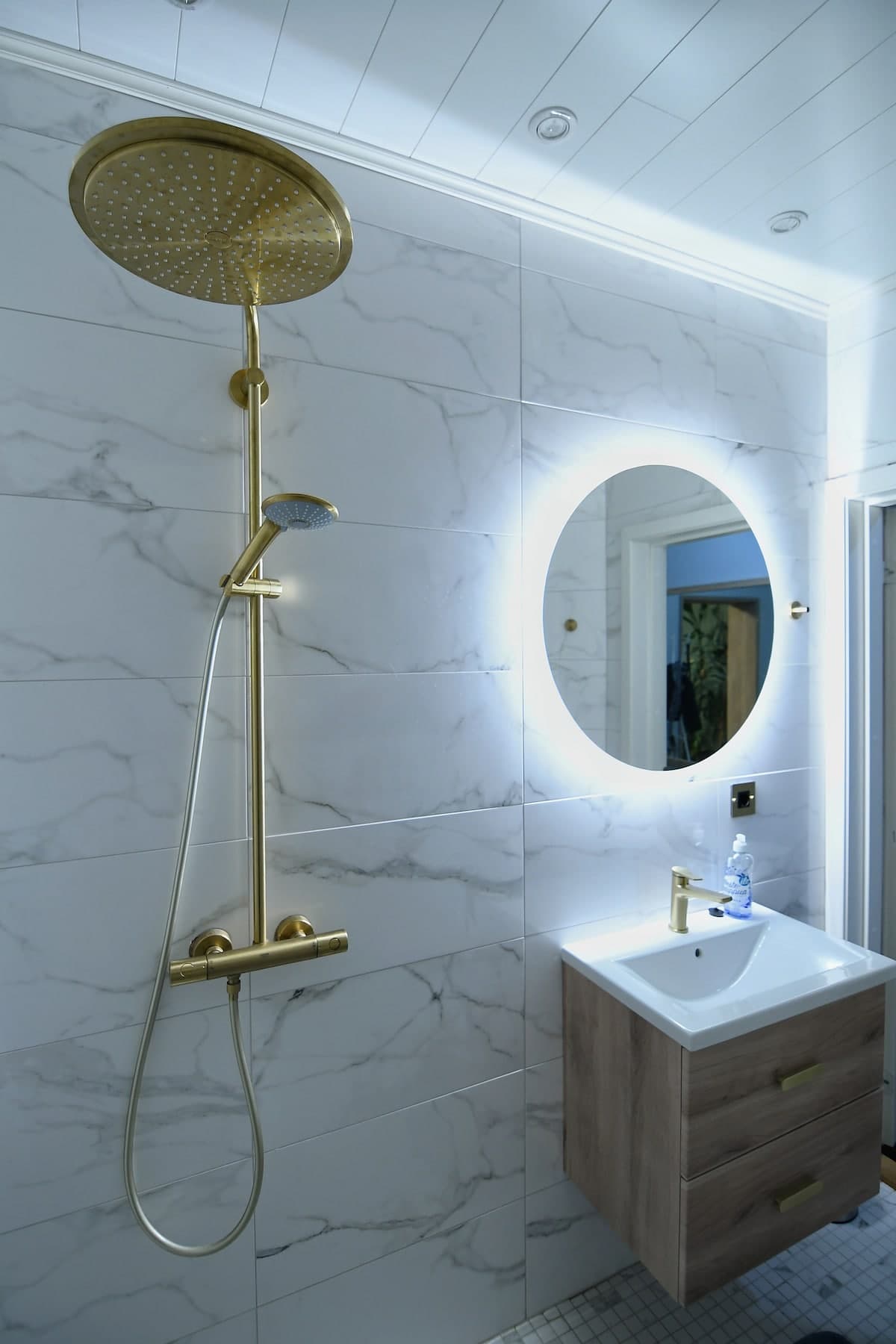 Brass rain shower with marble tiles and backlit round mirror